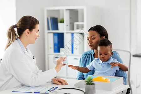医学,医疗保健儿科高加索医生给非裔美国人母亲婴儿儿子诊所服药医生诊所给儿子的女人吃药背景图片