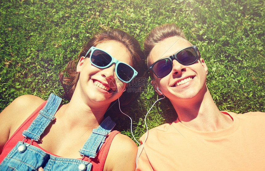 爱人的快乐的青少夫妇戴着太阳镜躺草地上,戴着耳机,夏天听音乐幸福的青少夫妇戴着耳机躺草地上图片