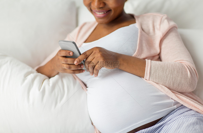 怀孕,人技术密切怀孕的非裔美国妇女与智能手机床上家家里智能手机的孕妇躺床上图片