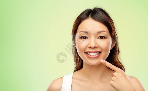 美丽人的快乐微笑的轻亚洲妇女指着她的嘴牙齿石灰绿色的自然背景快乐微笑的亚洲轻女人抚摸她的脸背景图片