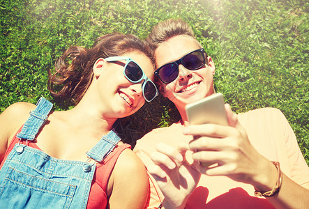 快乐的情侣戴着太阳镜躺草地上看手机图片