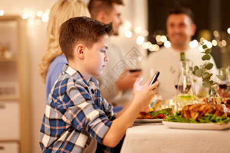 手机素材收集技术,假期人的快乐的男孩与智能手机家里举行家庭晚宴带智能手机的男孩家庭晚宴上背景