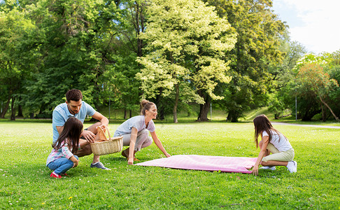 一家人在公园的草地上铺设野餐毯高清图片