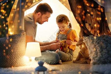 父亲与拿着泰迪熊玩具的小女儿在帐篷里玩玩具背景图片