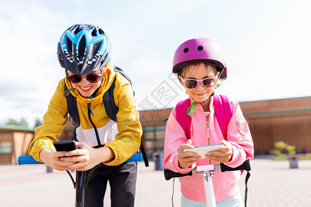 教育,童技术快乐的学校孩子戴着头盔,户外玩智能手机滑板车智能手机滑板车的学童背景图片