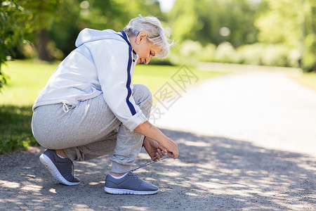 怎样系鞋素材健身,运动健康的生活方式老年女子夏季公园系鞋带夏季公园系运动鞋鞋带的老年女子背景