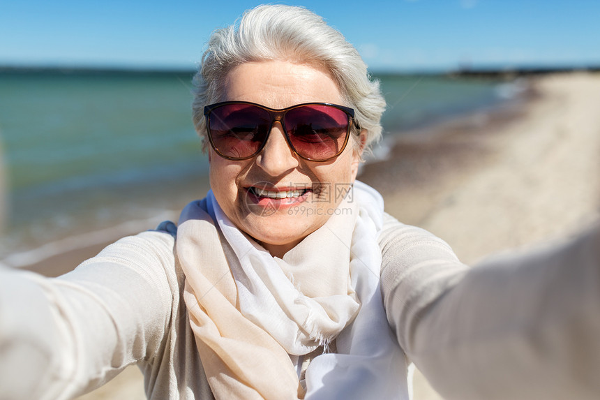 老人休闲快乐微笑的老妇女戴着太阳镜爱沙尼亚海滩自拍戴太阳镜的高级女人海滩上自拍图片