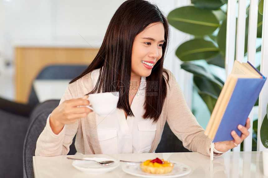 人与休闲的微笑的亚洲女人喝咖啡与甜点读书咖啡馆女人咖啡馆喝咖啡看书图片