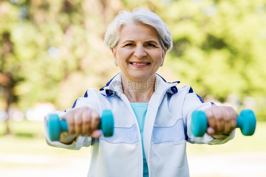 健身,运动健康的生活方式快乐的微笑老妇女与哑铃锻炼夏季公园戴哑铃的老妇女公园锻炼图片