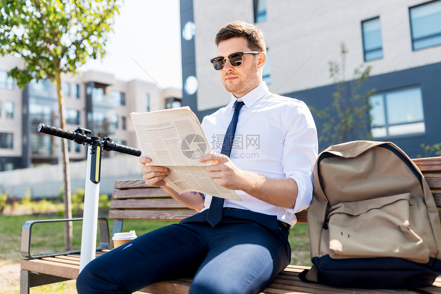 商业新闻企业人士轻的商人带着袋子,电动滑板车城市的街道长凳上阅读报纸商人与滑板车阅读报纸城市图片
