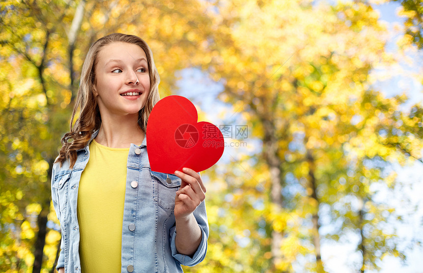 爱人的微笑的漂亮少女穿着牛仔夹克抱着红色的心秋天的公园背景微笑的十几岁女孩,红色的心秋天的公园图片