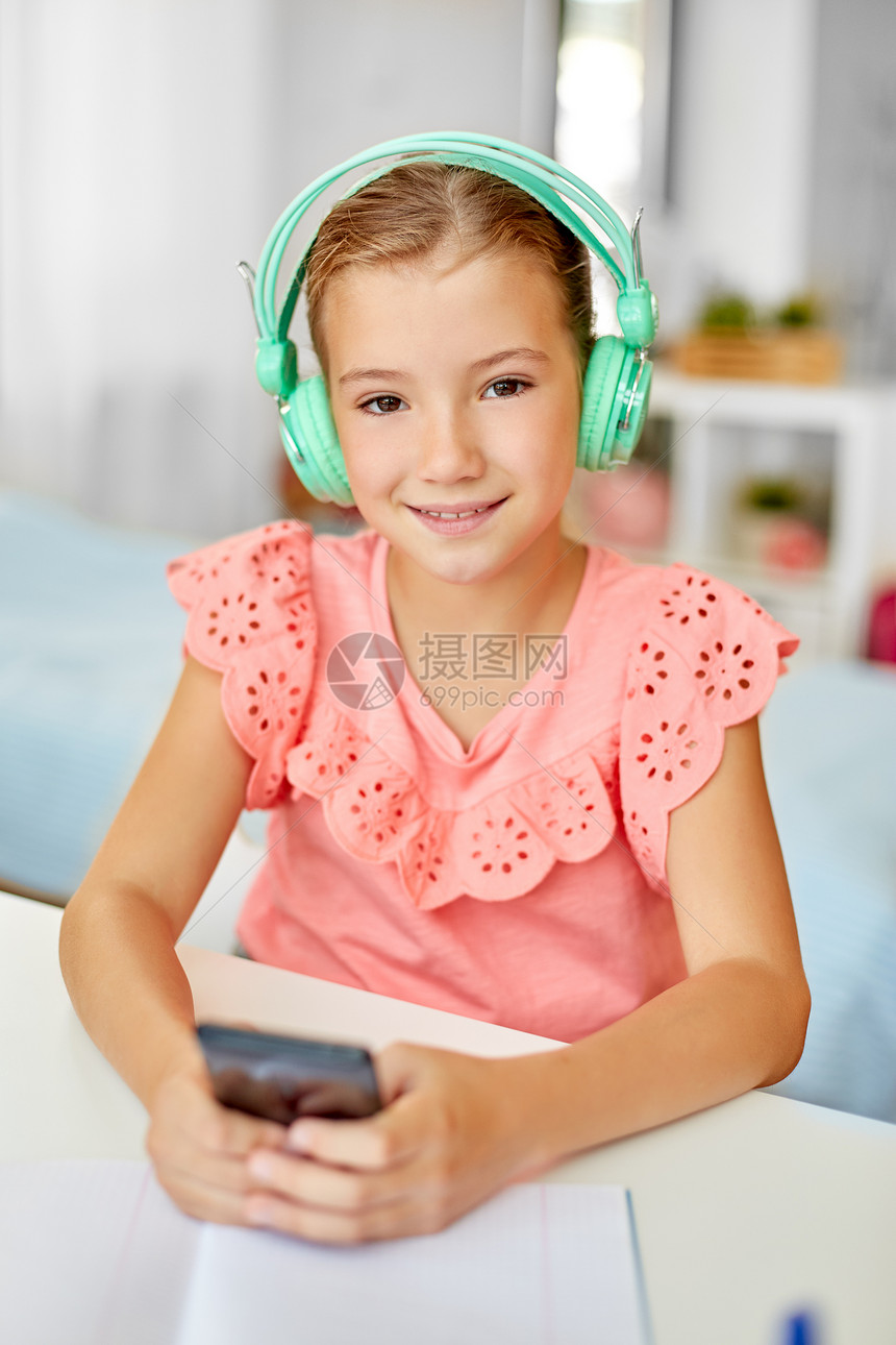 儿童,休闲技术快乐的学生女孩耳机与智能手机听音乐家里的办公桌戴耳机的女孩手机上听音乐图片