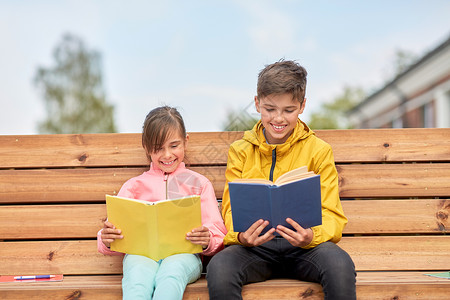 教育,童人的快乐的学校孩子兄妹阅读书籍,坐木制的街道长凳户外学校的孩子们坐长凳上看书背景图片