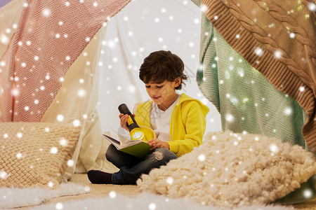 童,诞节人们的快乐的男孩阅读书与火炬灯孩子帐篷帐篷家里的雪快乐的男孩家孩子们的帐篷里看书背景图片