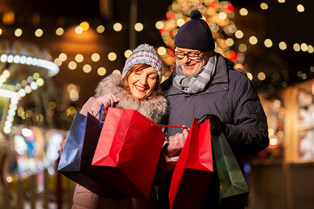 销售,寒假人们的快乐的老夫妇带着购物袋诞市场纪念品商店塔林市政厅广场,爱沙尼亚诞市场上的老夫妇带着购物袋背景图片