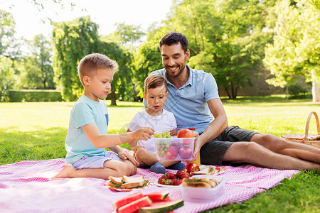 野餐三明治点心家庭休闲父爱的快乐的父亲两个小儿子夏季公园野餐快乐的家庭夏天的公园野餐背景