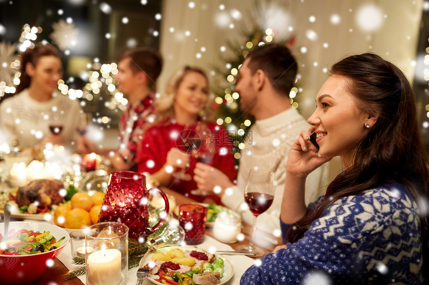 假期,沟通庆祝快乐的轻女人打电话给智能手机,并雪地上朋友吃诞晚餐诞节晚餐时打电话给智能手机的女人图片