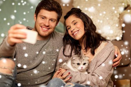 猫照片诞节,技术人的快乐的夫妇与猫雪地上用智能手机自拍幸福的夫妇家里用智能手机自拍背景