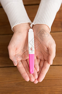 生育生育女手着阳妊娠试验,木板背景上两条条纹妇女手握妊娠试验阳图片