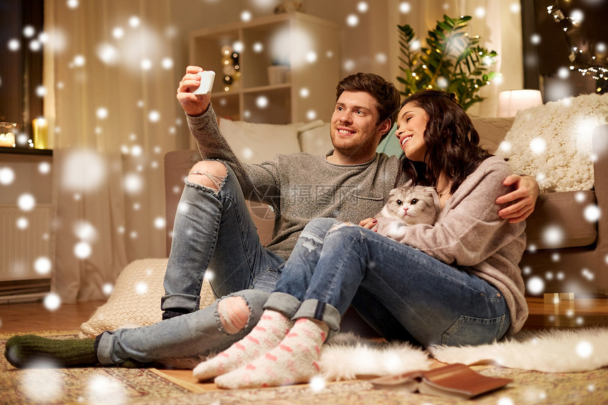 诞节,技术人的快乐的夫妇与猫雪地上用智能手机自拍幸福的夫妇家里用智能手机自拍图片