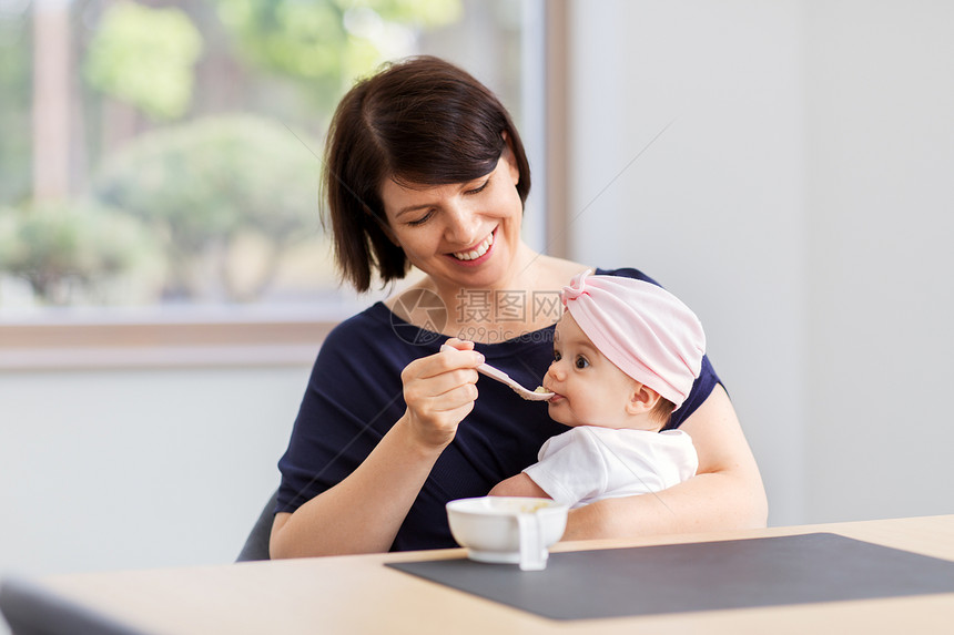 婴儿期,母亲食物的快乐的中母亲勺子喂养婴儿的女儿与纯净家里中母亲家喂婴儿女儿图片