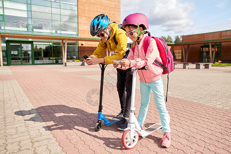 教育,童技术快乐的学校孩子戴着头盔,户外玩智能手机滑板车智能手机滑板车的学童背景图片