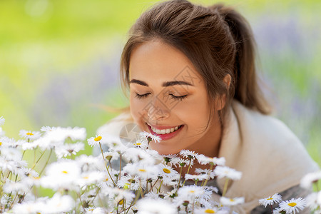 园艺人们的快乐的轻女人闻洋甘菊花夏季花园靠近闻洋甘菊花的女人背景图片
