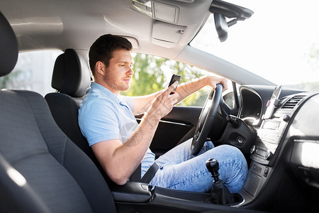 微笑的司机驾驶汽车用智能手机背景图片