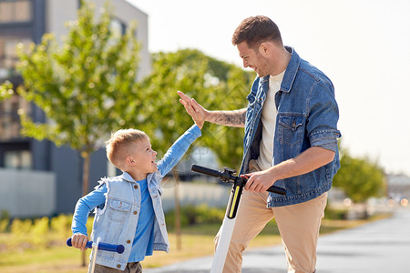 快乐的父亲和小儿子踩着滑板车了击掌背景图片