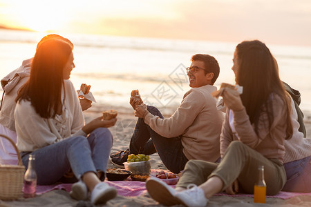 快乐的朋友海滩野餐时吃三明治图片