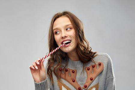诞节,人节日的快乐的轻女人穿着毛衣,用驯鹿图案吃糖果拐杖穿诞毛衣的女人吃糖果拐杖背景图片