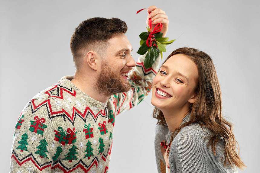 诞节,人们节日传统的幸福的夫妇毛衣亲吻槲寄生灰色背景下的肖像幸福的夫妇槲寄生下接吻图片