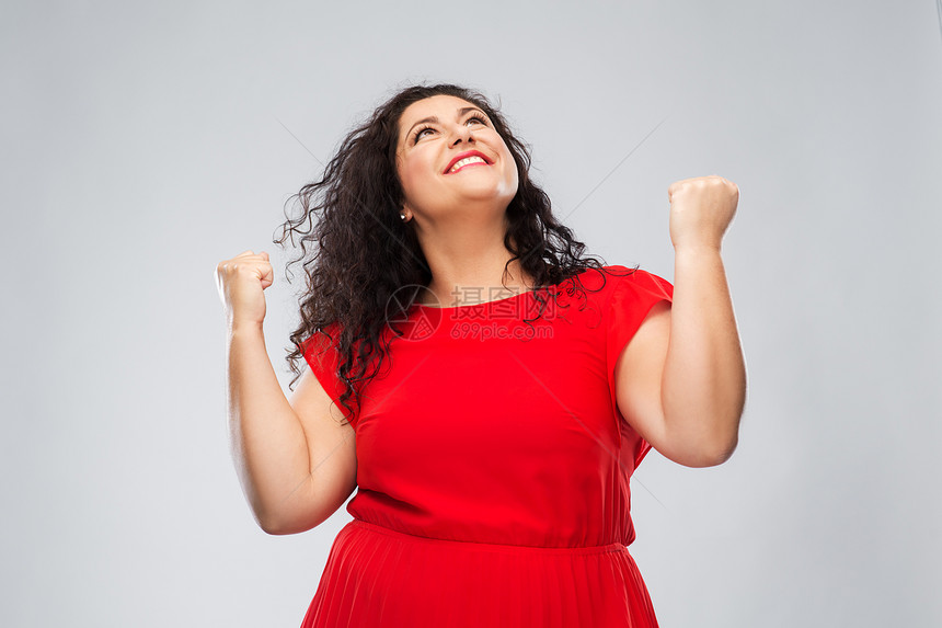 情感,手势成功的快乐的女人穿着红色的衣服抬头,灰色的背景上挥舞拳头穿着红色连衣裙的快乐女人庆祝成功图片