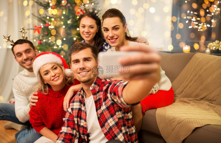 庆祝假期快乐的朋友戴着眼镜,家里的聚会上庆祝诞节,用智能手机自拍朋友们庆祝诞节自拍图片