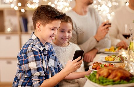 手机素材收集技术,假期人的快乐的男孩妹妹用智能手机家里举行家庭晚宴带妹妹的男孩家庭晚餐时用智能手机背景