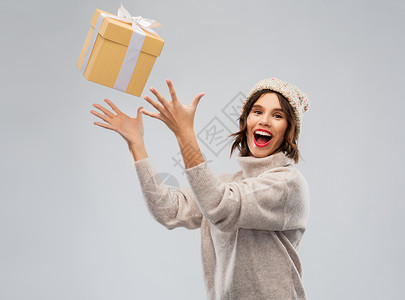 跳跃者灰色诞节,假日人们的快乐的微笑轻女子针冬帽毛衣捕捉礼品盒灰色背景戴冬帽的轻女子接球礼盒背景