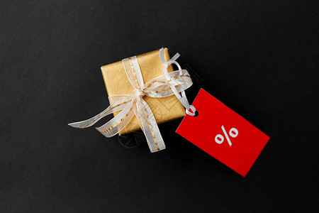 销售,假日诞节小黄金礼品盒红色折扣标签与百分比标志黑色背景小礼品盒红色销售标签与折扣标志背景图片