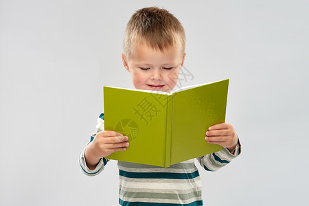 学校,教育儿童微笑的小男孩灰色背景下阅读书籍的肖像微笑男孩读书的肖像图片