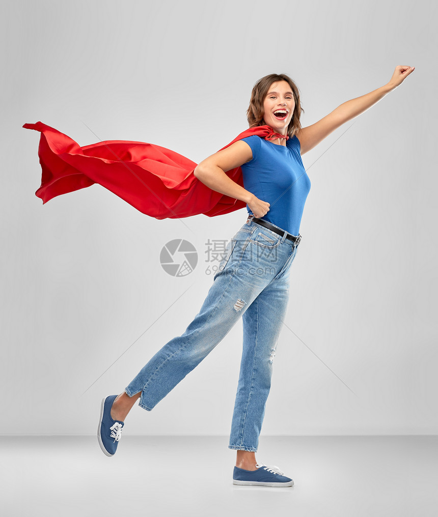 女人的力量人的快乐的女人穿着红色超级英雄斗篷,灰色背景上飞行姿势穿着红色超级英雄斗篷的快乐女人图片