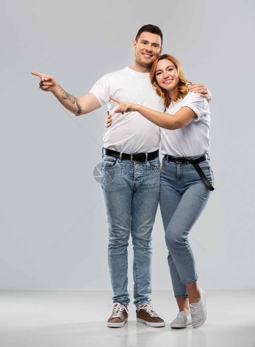 关系人的幸福夫妇的肖像白色T恤给些灰色背景穿着白色T恤的幸福夫妇指着手指图片