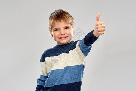 童,手势人的微笑的小男孩条纹套头衫拇指灰色背景穿条纹套衫的小男孩竖大拇指背景图片