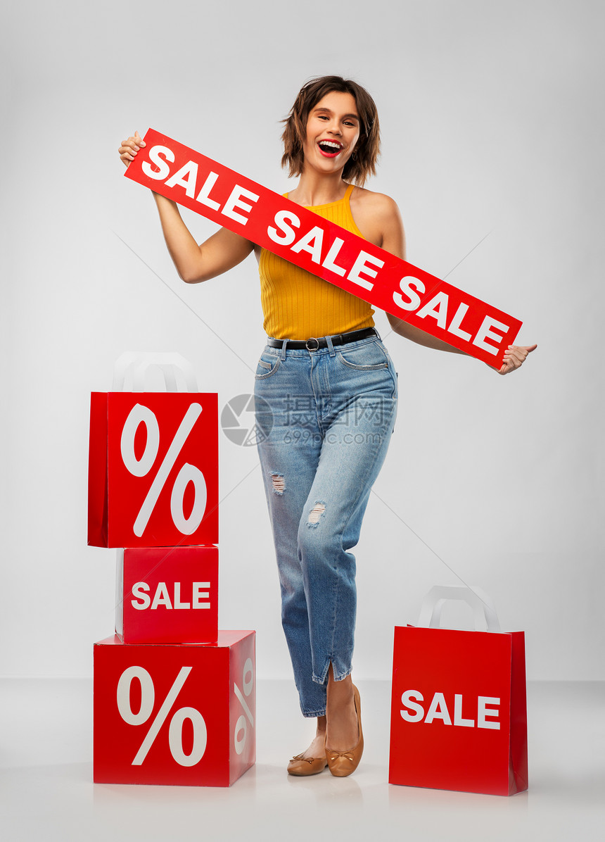 销售,消费主义人们的快乐的微笑轻妇女芥末黄色上衣牛仔裤与购物袋灰色背景带着购物袋的快乐微笑的轻女人图片