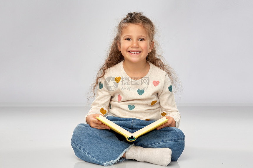 阅读,教育童的美丽的微笑女孩坐地板上,阅读灰色背景的书漂亮的微笑女孩地板上看书图片