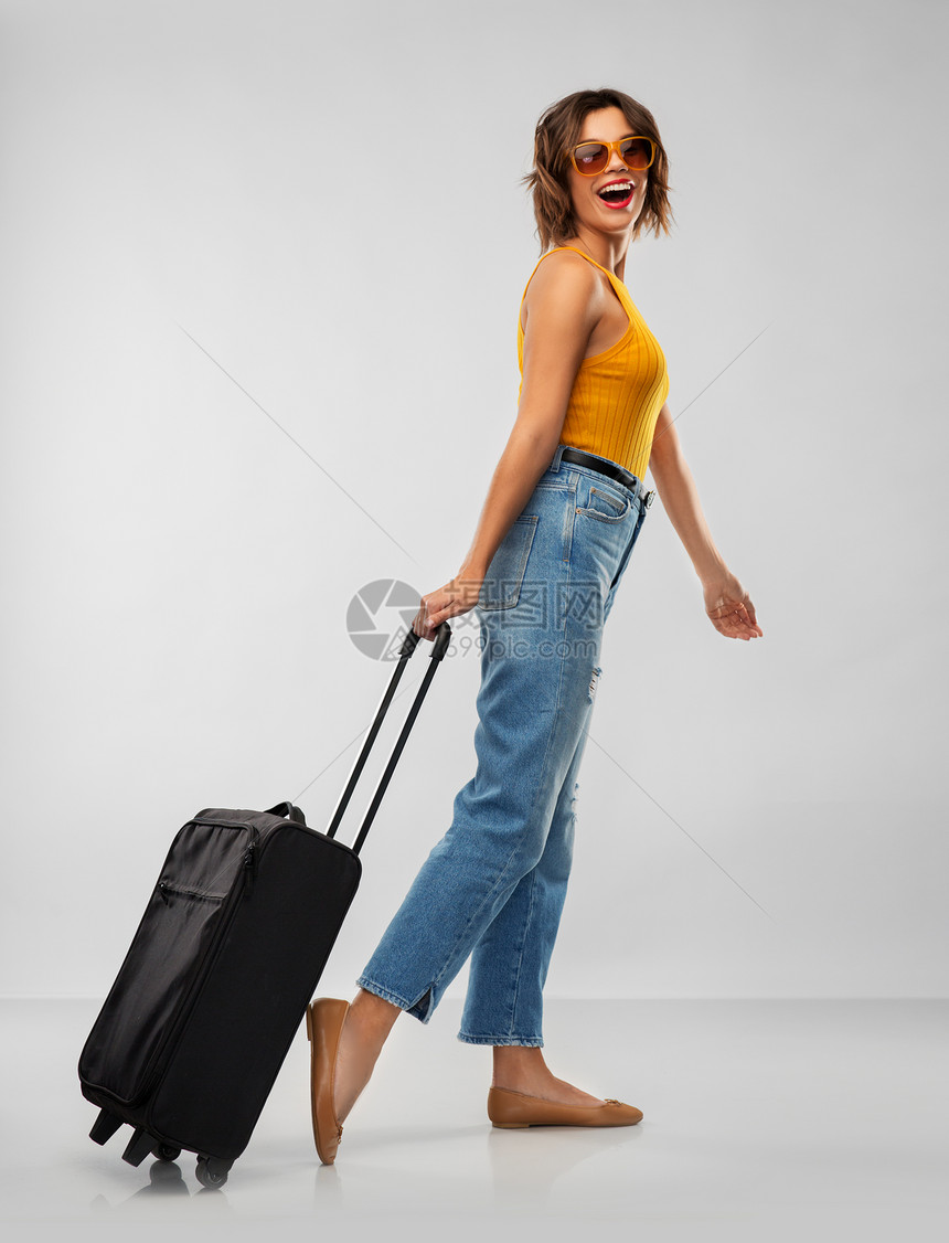 旅行,旅游度假的快乐的笑轻妇女芥末黄色顶部与携带包灰色背景戴太阳镜带旅行袋的快乐轻女人图片