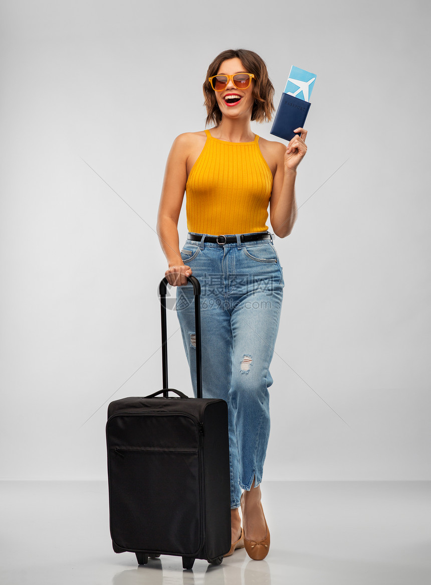 旅行,旅游度假的快乐的笑轻芥末黄色顶部与机票,护照随身携带的灰色背景带着机票旅行袋的快乐轻女人图片