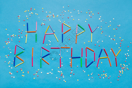 五彩糖果节日,庆祝派单词生日快乐,由彩色蜡烛星形糖洒蓝色背景上用蓝色蜡烛的生日快乐的话设计图片