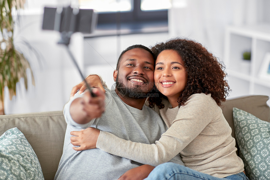 家庭技术人的快乐的非裔美国人夫妇家里用智能手机自拍棒拍照夫妇家里用自拍杆拍照图片