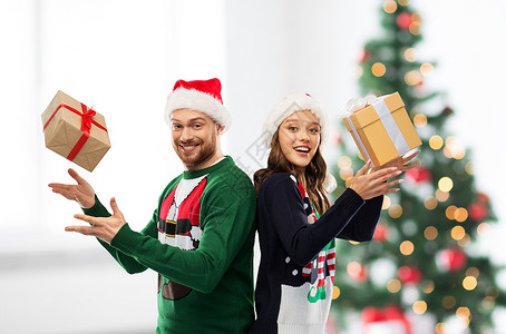 人们节日的幸福的夫妇戴着诞老人的帽子,毛衣派上诞树灯背景诞毛衣里的幸福夫妇带着礼物背景图片