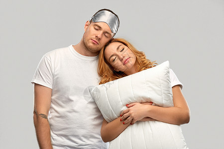人际关系人的夫妇穿着白色T恤,戴着眼罩灰色背景的枕头夫妇带着眼罩枕头图片
