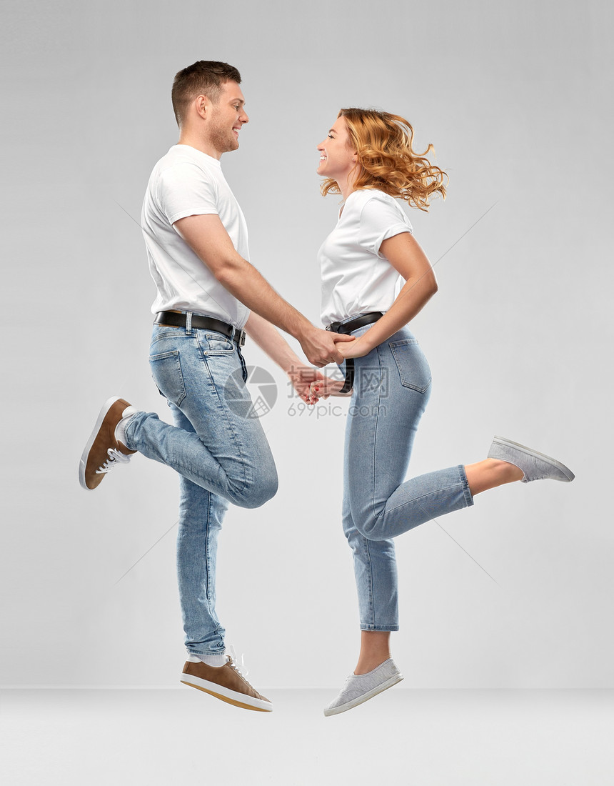关系人的幸福的夫妇穿着白色T恤跳过灰色背景穿着白色T恤衫的快乐夫妇跳着图片